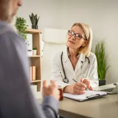 Lekarka w białym kitlu rozmawia z pacjentem, notując coś na kartce. Podkreśla, ile ważne jest skierowanie do specjalisty.